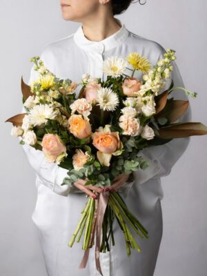 Rose pesca, garofani chiari, violaciocca crema, germini spider bianchi e gialli, roselline ramificate chiare e verde di stagione nel Bouquet Luce