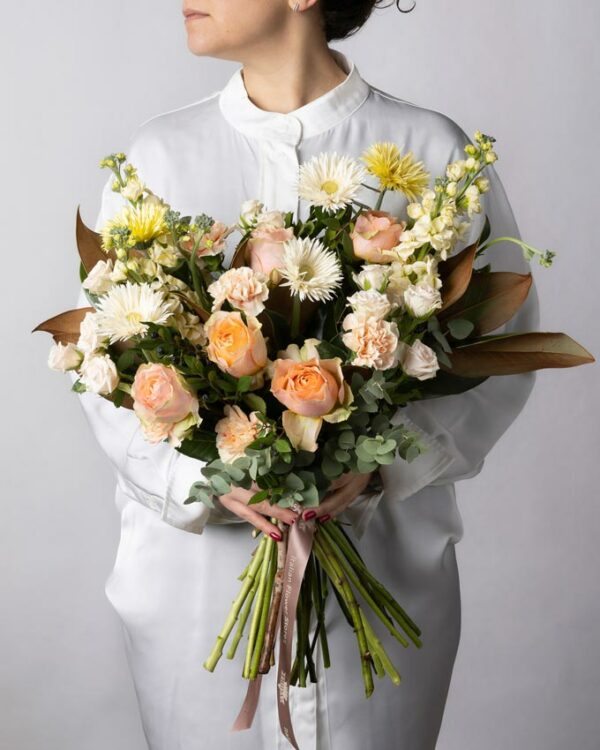 Rose pesca, garofani chiari, violaciocca crema, germini spider bianchi e gialli, roselline ramificate chiare e verde di stagione nel Bouquet Luce
